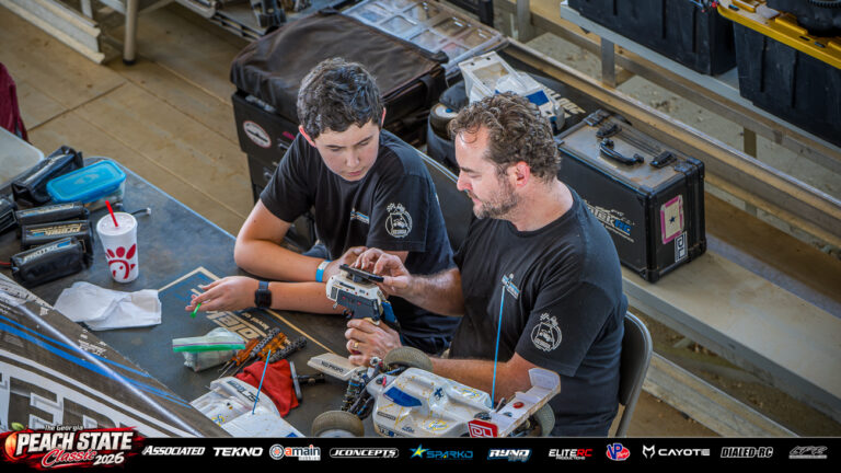 Two racers review a radio transmitter beside a nitro buggy and tools at a pit table at the 2026 Georgia Peach State Classic. A candid moment from the race weekend’s Good Times photo gallery.