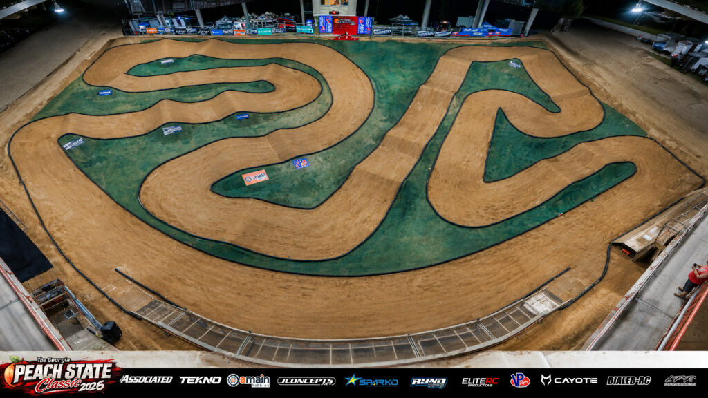 Overhead photograph of the complete dirt RC track layout built by Brian Burnette for the 2026 Georgia Peach State Classic. The covered course features jumps, sweeping corners and tight turns separated by black pipe barriers and green infield areas.