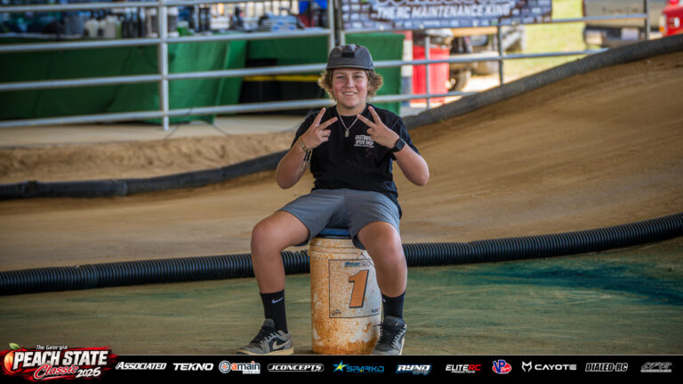 A smiling turn marshal flashes two peace signs while seated on the number one marshal bucket beside the dirt track at the 2026 Georgia Peach State Classic. A candid moment from the race weekend’s Good Times photo gallery.